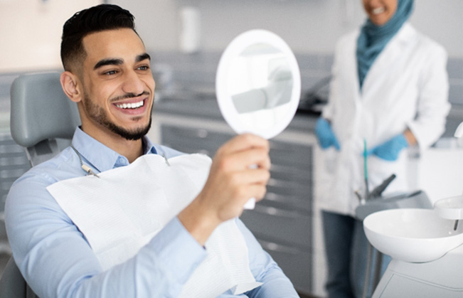 Man in dental chair smiling at reflection in mirror with dentist in the background